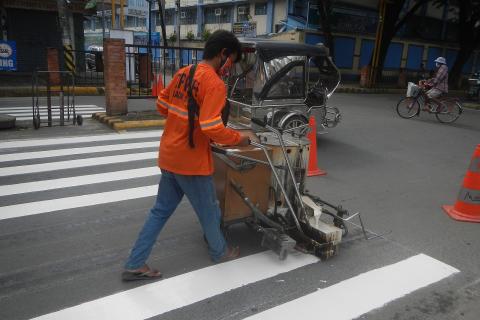 A worker painting a zebra crossing. The Thai for "a worker painting a zebra crossing" is "คนงานกำลังทาสีทางม้าลาย".