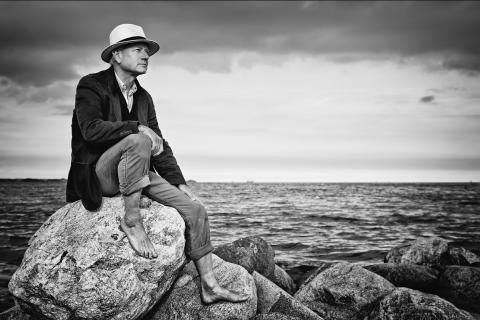 A man sitting on a rock. The Thai for "a man sitting on a rock" is "ผู้ชายนั่งบนโขดหิน".