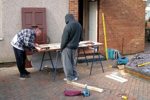 Two carpenters repairing a door. The Thai for "two carpenters repairing a door" is "ช่างไม้สองคนกำลังซ่อมประตู".